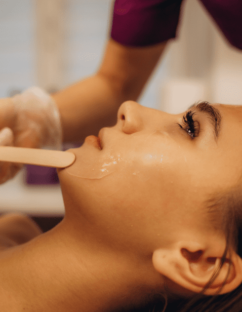 Esthetician applying warm wax to a woman's chin during a professional chin waxing treatment at a spa.