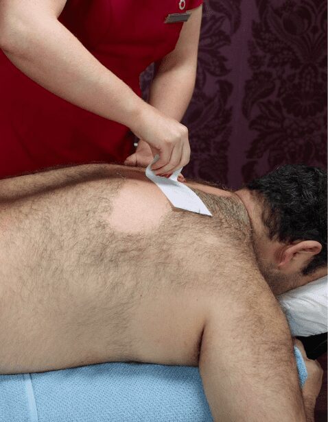 A man receiving a full back waxing treatment at a spa, with a professional esthetician using a waxing strip to remove hair in a swift motion for smooth, hair-free skin.
