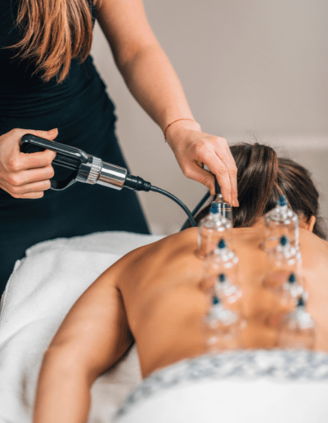 Therapist performing lymphatic cupping massage on a client's back using vacuum suction cups to stimulate lymph flow and promote detoxification.