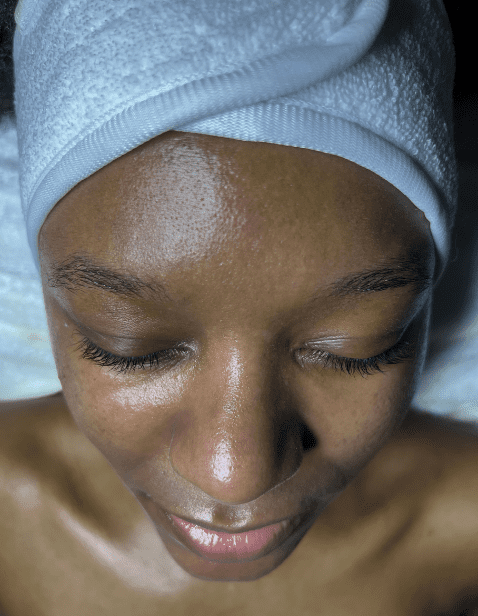 Close-up of a woman with glowing, smooth skin and closed eyes, wearing a white headband after an Vitamin C Glow Facial.