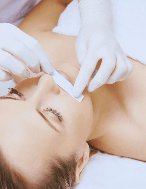Woman receiving upper lip waxing treatment with a white wax strip applied by a professional wearing gloves.