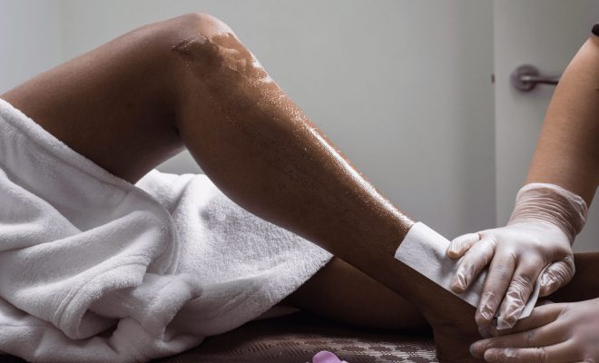 Esthetician applying a waxing strip to a client’s lower leg during a professional hair removal session at a spa.