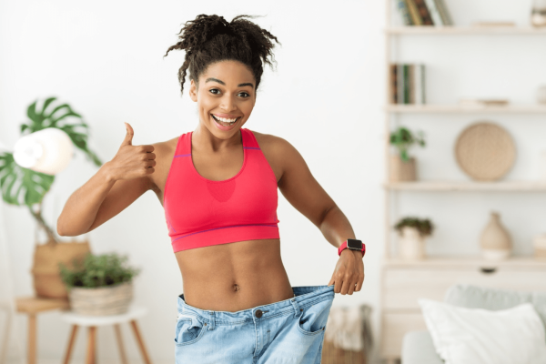 Smiling woman showing significant weight loss results by holding loose-fitting jeans after GLP-1 weight management treatment.