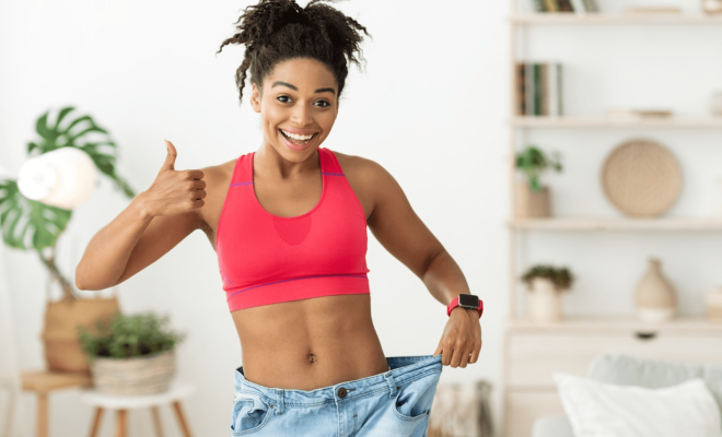 Smiling woman showing significant weight loss results by holding loose-fitting jeans after GLP-1 weight management treatment.