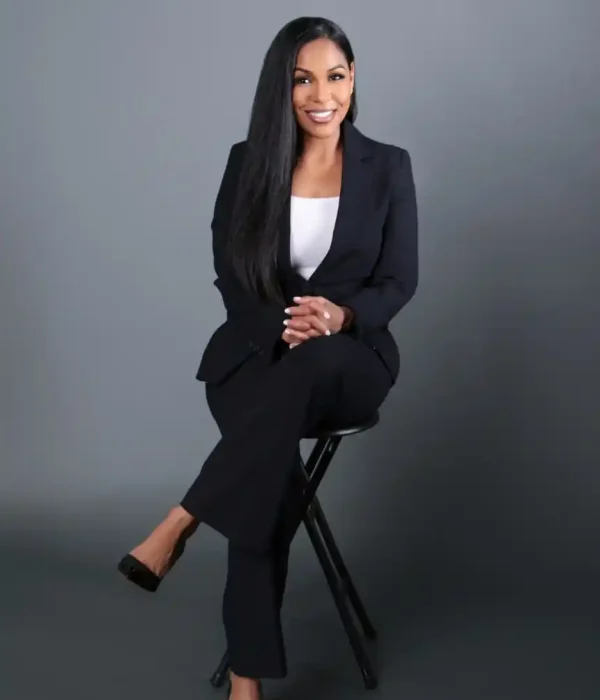 Professional portrait of Jonel Feliciano, founder of Isle of Indulgence Spa, wearing a black blazer and white top, smiling confidently with arms crossed against a blurred natural background.